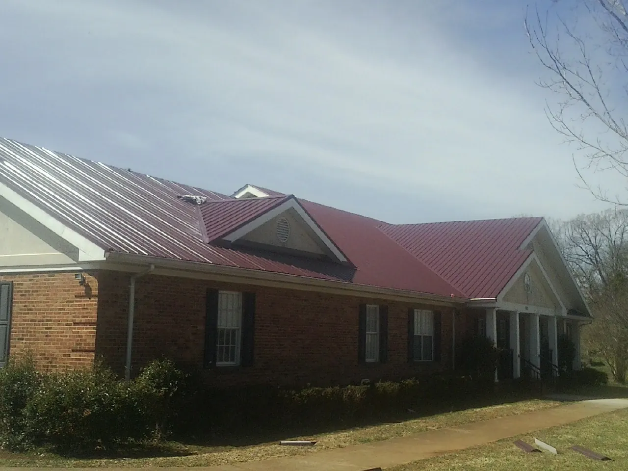 Red metal roof with gabled entries on a long brick building, from a Hail Damage Roof Repair job in Forest Grove