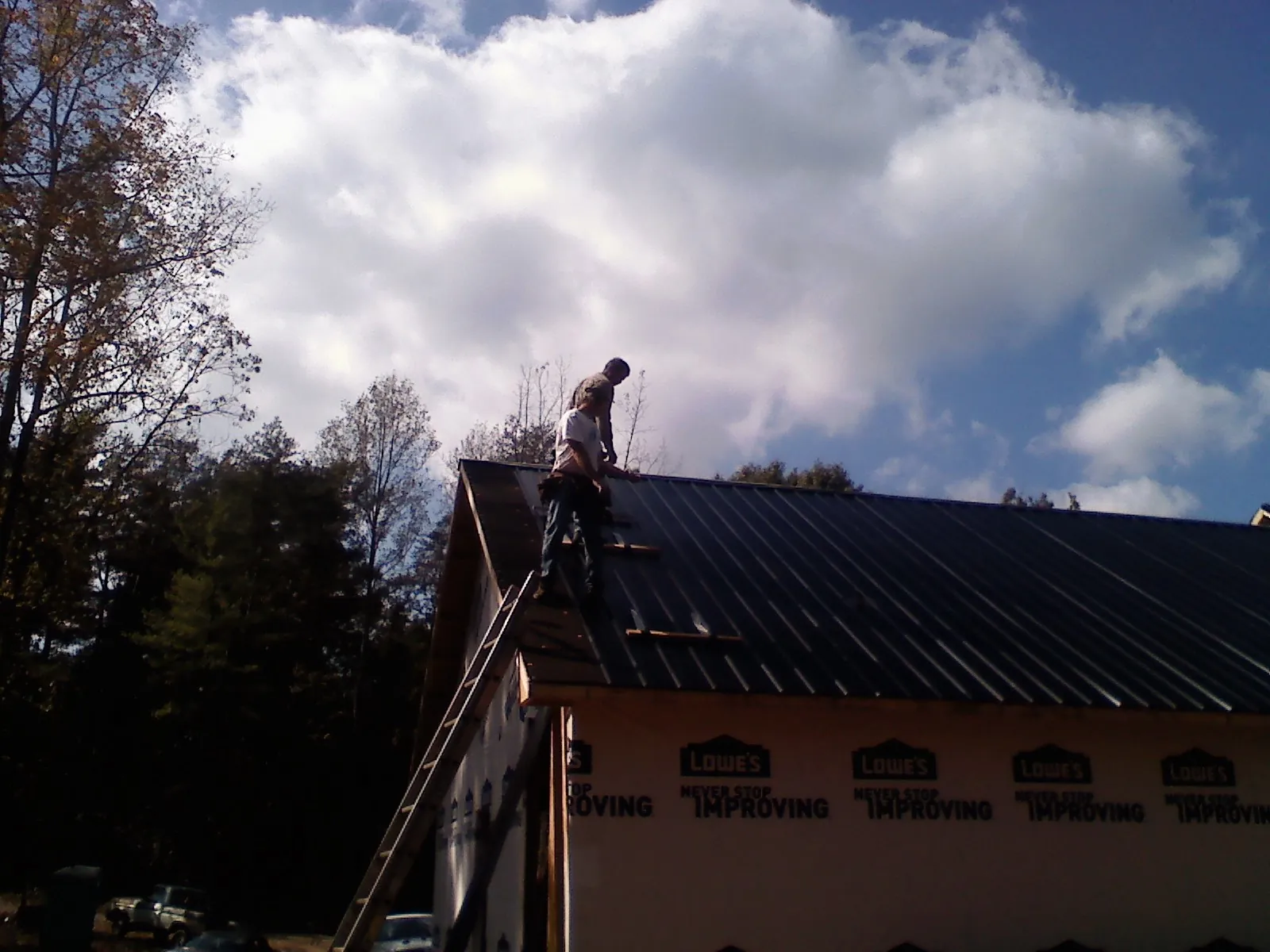 Roofer fastening dark metal panels high against a cloudy sky, from a Roof Inspection job in Forest Grove