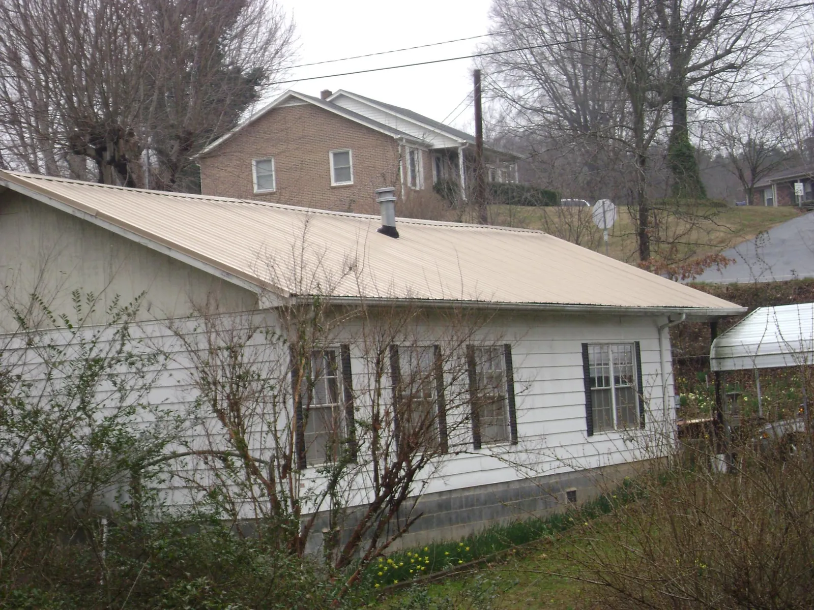 Tan metal roof on a white sided house set into a hillside — Commercial Roofing by Roofing Brothers in Forest Grove